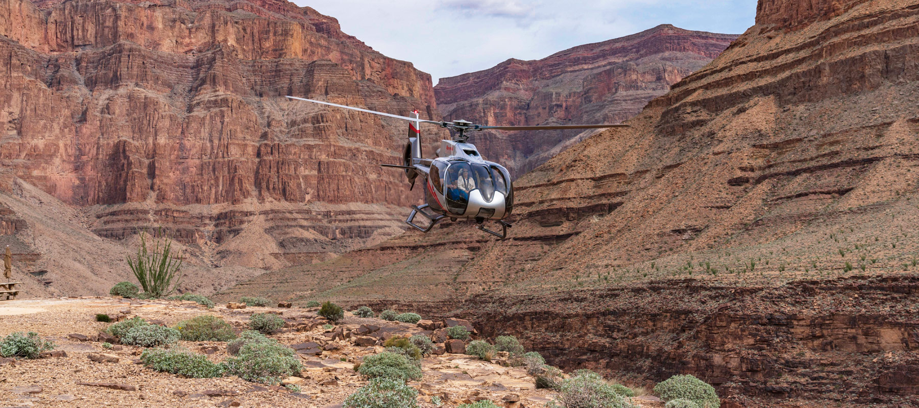Helicopter approaching a landing area surrounded by the Grand Canyon’s red rock cliffs